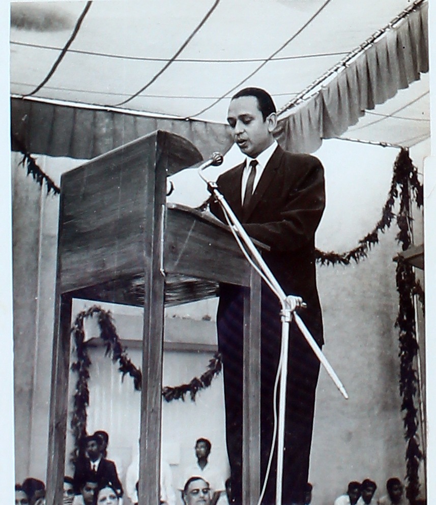 A man speaking from a podium beneath a shamiana.